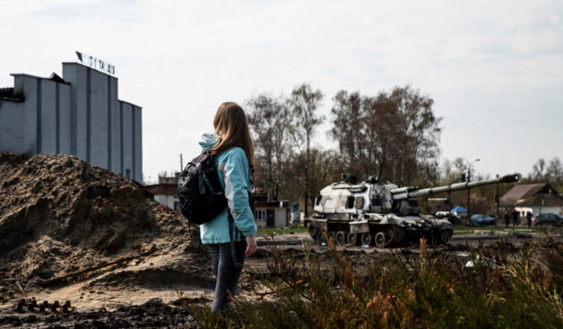 Jugendliche mit Rucksack steht auf einem verwüsteten Gelände mit aufgeworfener Erde und Schutt, während im Hintergrund ein zerstörter Panzer und ein Industriegebäude zu sehen sind – symbolisiert die Auswirkungen von Krieg und Zerstörung auf den Alltag und die Bedeutung von Frieden.