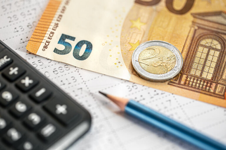 Nahaufnahme von Euro-Geldscheinen (50-Euro-Schein) und Münzen (2-Euro-Münze) neben einem Taschenrechner und einem Stift auf einem Buchhaltungsformular – Symbolbild für Budgetplanung und Finanzmanagement.
