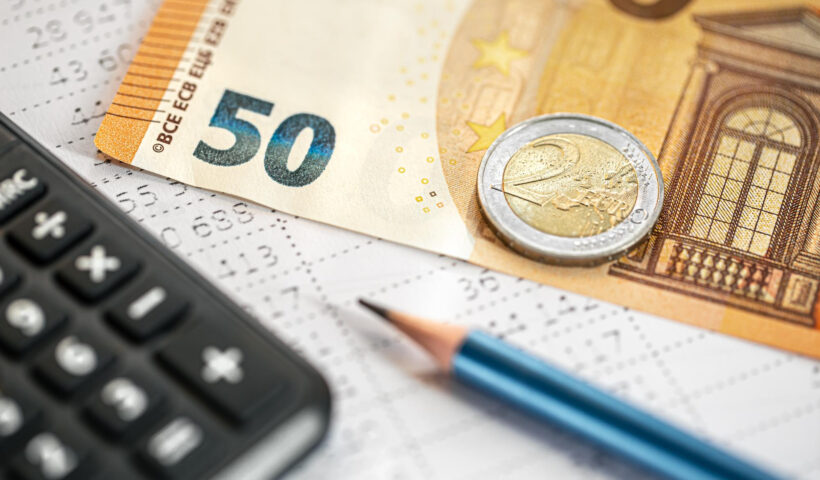 Nahaufnahme von Euro-Geldscheinen (50-Euro-Schein) und Münzen (2-Euro-Münze) neben einem Taschenrechner und einem Stift auf einem Buchhaltungsformular – Symbolbild für Budgetplanung und Finanzmanagement.